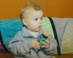 Petit Boum Spiral Pink and Spiral Blue sensory bottles lifestyle image of a child holding the bottles with a colorful play tunnel in the background