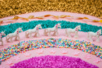 Petit Boum Sensory Bottle Unicorn lifestyle image featuring white unicorn figurines arranged in a rainbow pattern of colorful beads on a pink background