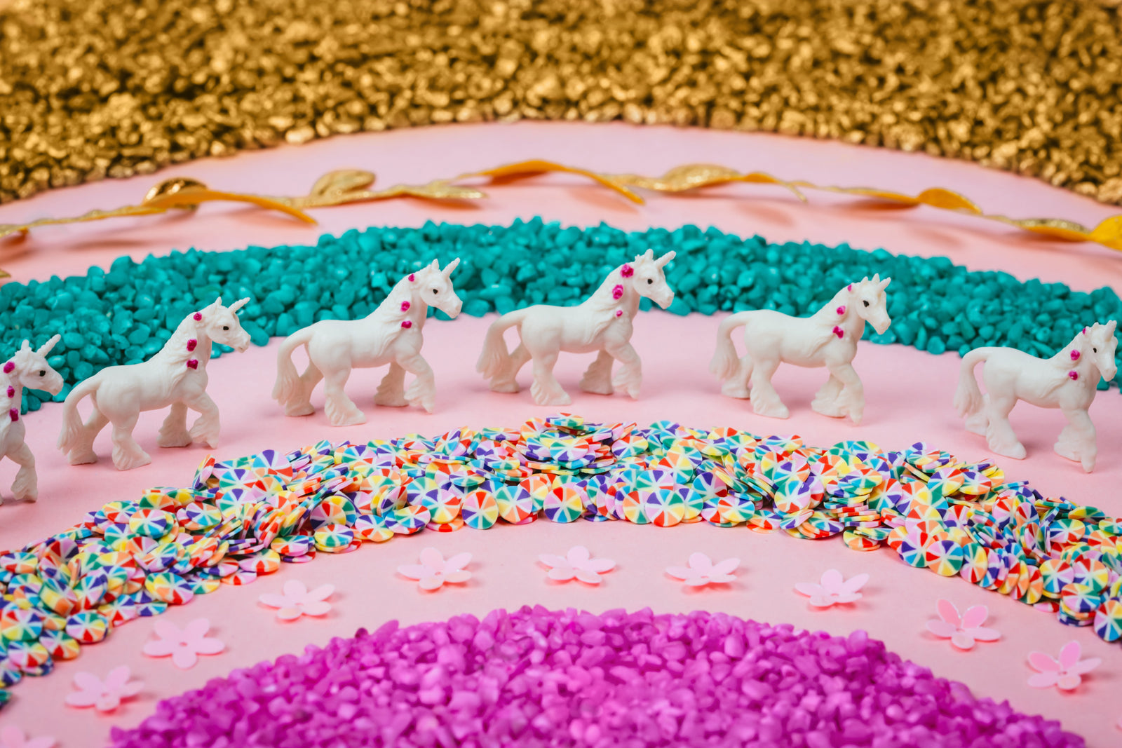 Petit Boum Sensory Bottle Unicorn lifestyle image featuring white unicorn figurines arranged in a rainbow pattern of colorful beads on a pink background