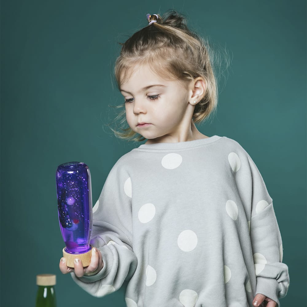 Child holding a Petit Boum Magic sensory bottle against a teal background