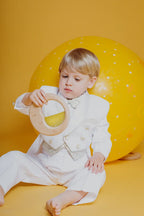Lifestyle image of a child in a white outfit holding the Petit Boum sensory Moon against a yellow background