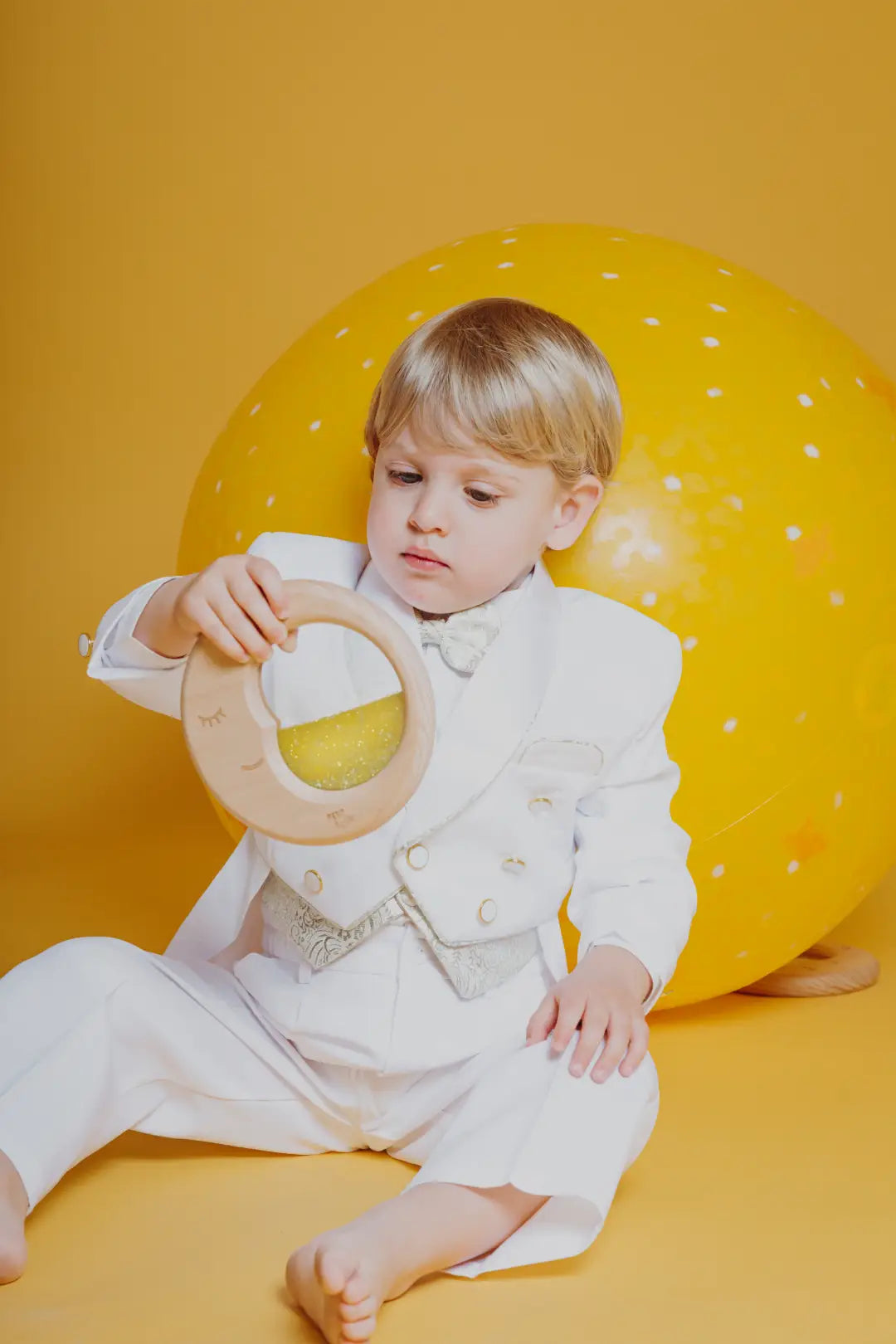 Lifestyle image of a child in a white outfit holding the Petit Boum sensory Moon against a yellow background
