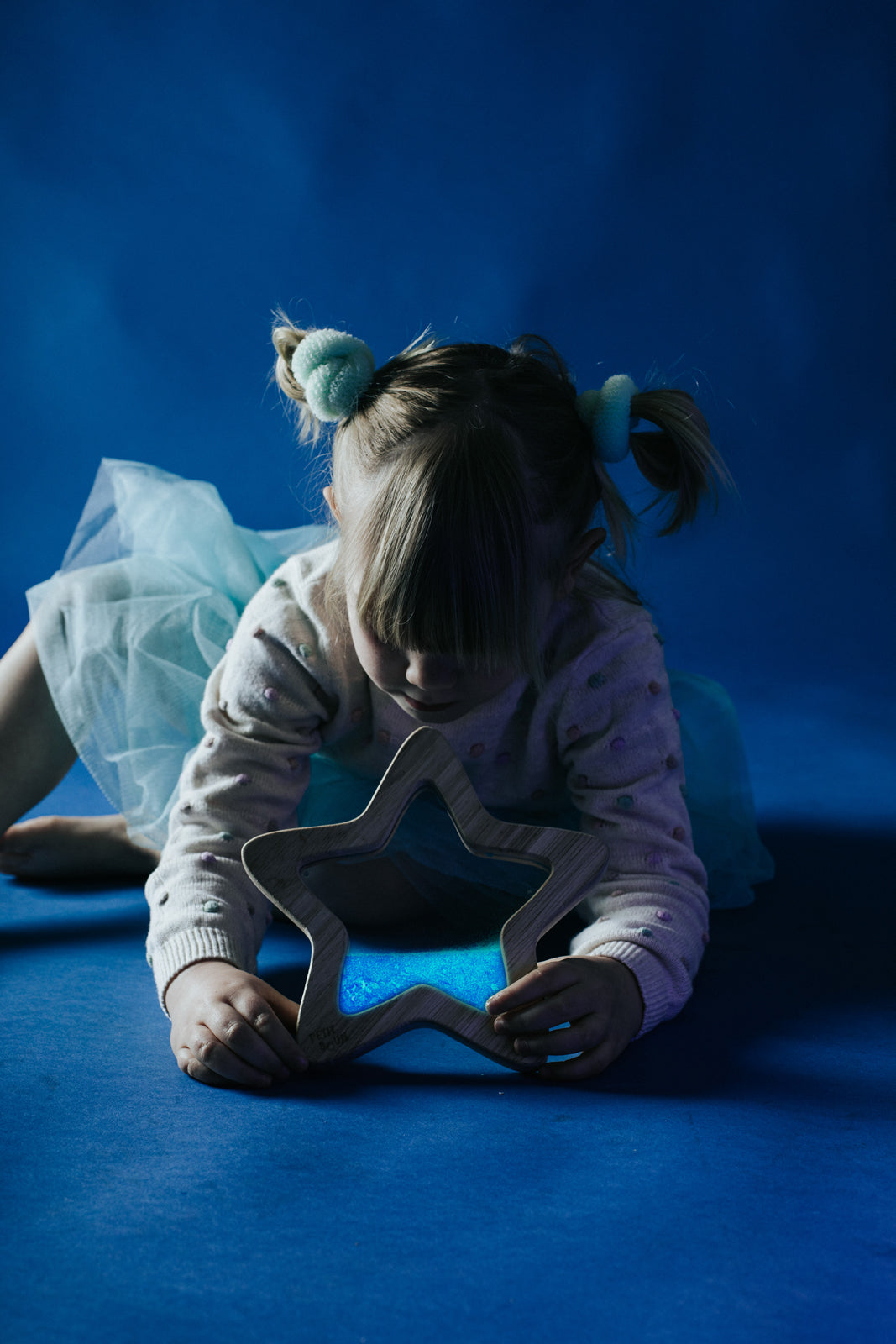 Petit Boum sensory star Orionis lifestyle image of a girl lying down holding the bottle in front of her in a dark room, showing the glow-in-the-dark effect of the sensory star