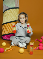 Petit Boum Spiral Pink sensory bottle lifestyle image of a girl holding two pink spiral bottles amid a colorful play tunnel and scattered play balls